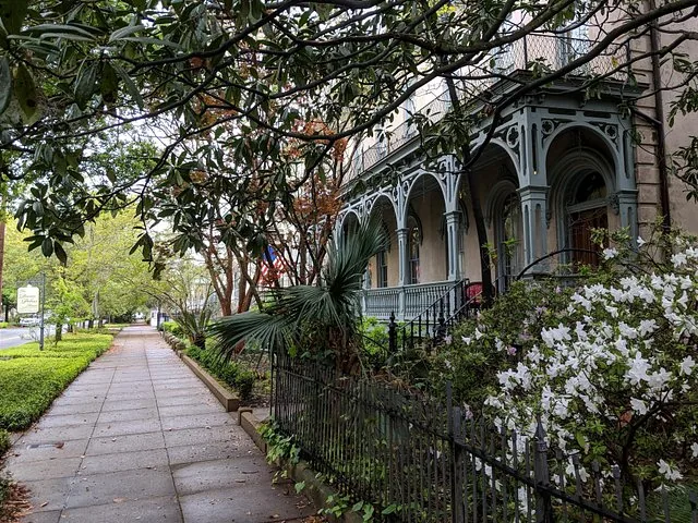 A sidewalk passing by a historic home with intricate balconies in Savannah.
