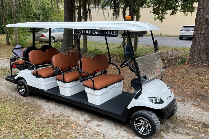 Ein großer, weißer Golfcart für mehrere Personen, im Freien neben Bäumen geparkt.