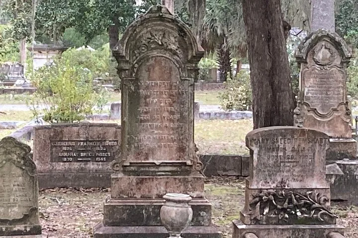 Several old stone grave markers in a grassy, tree-filled cemetery.