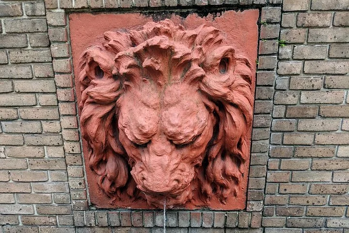 Une sculpture de tête de lion en terre cuite fixée sur un mur de briques, avec un filet d'eau qui ruisselle.