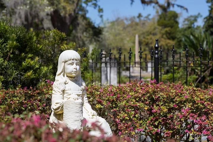 Weiße Marmorstatue eines jungen Mädchens in einer Gartenanlage.